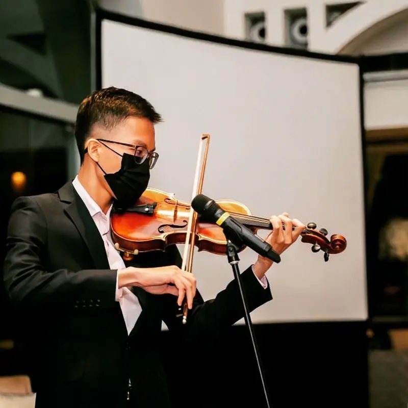 Violinist in a black suit playing a solo into a microphone at an evening event in Singapore