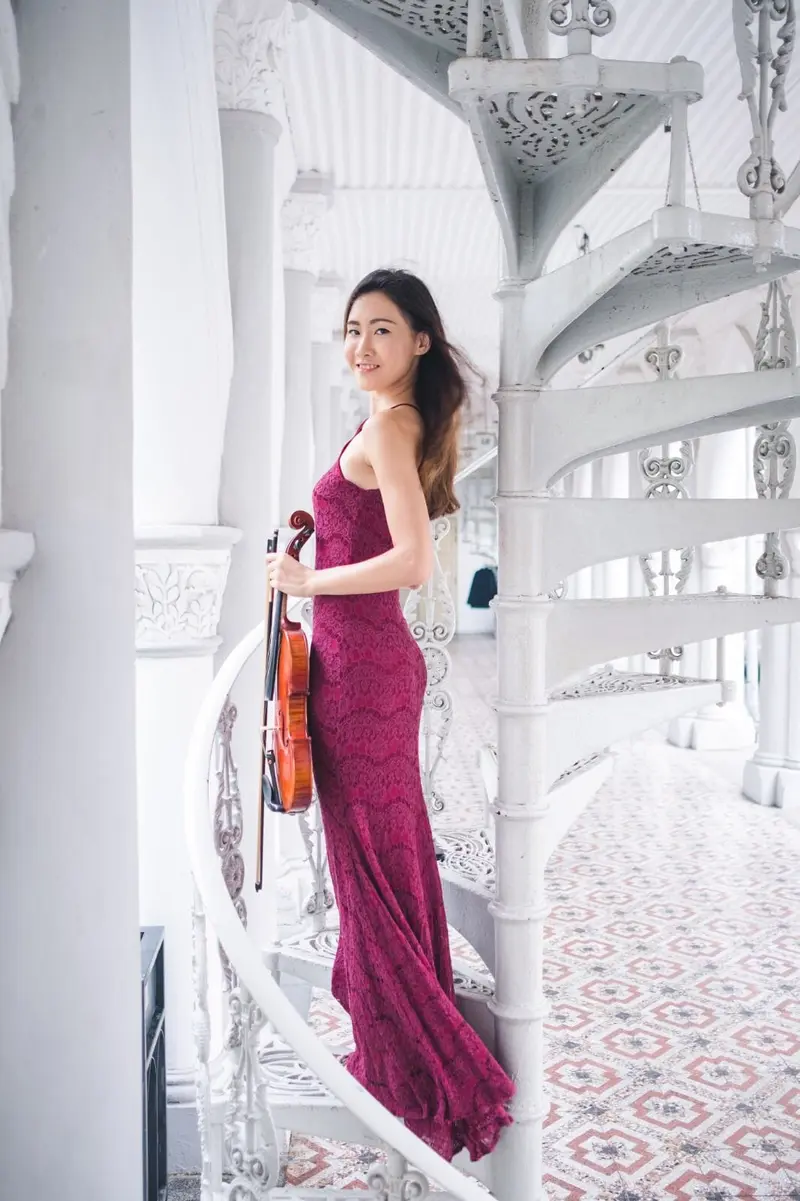 Violinist in a long burgundy gown holding her violin on a white spiral staircase