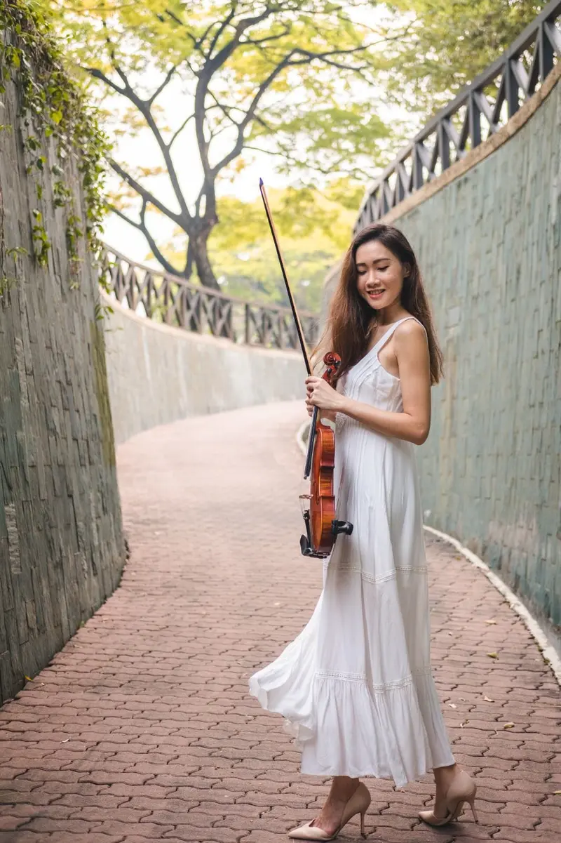 Violinist in a white dress with her violin and bow on a tree lined garden path in Singapore